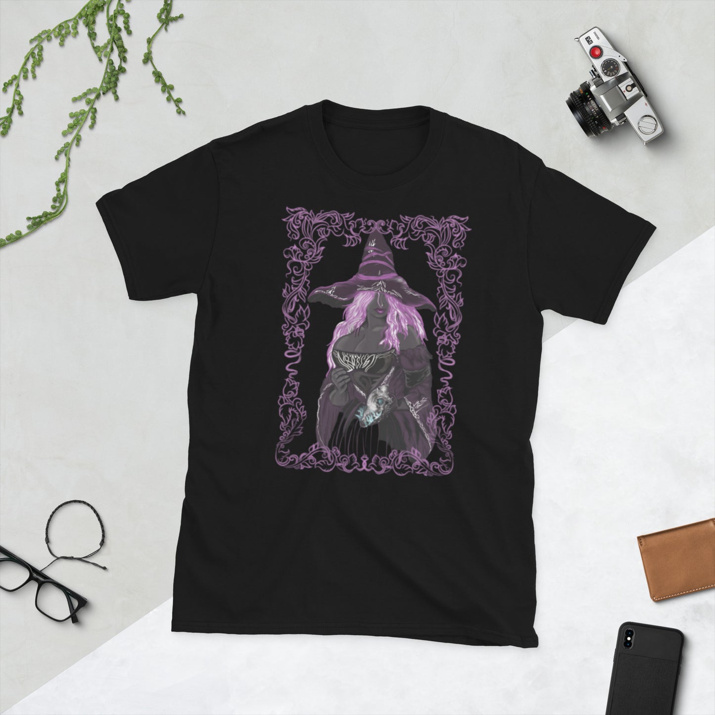 Black t-shirt with a purple graphic of a witch on a white surface with a camera and phone.